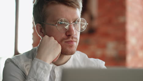 anxious-and-pensive-man-is-reading-news-in-laptop-sitting-in-cafe-closeup-portrait-of-attractive-guy-with-glasses